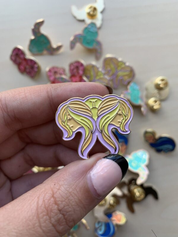 Gemini Pin in pastel colors and gold enamel held by hands.