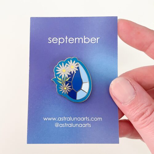September birth pin. Gold enamel pin with sapphire and aster flower design. Pin set in card labeled september by astraluna arts.